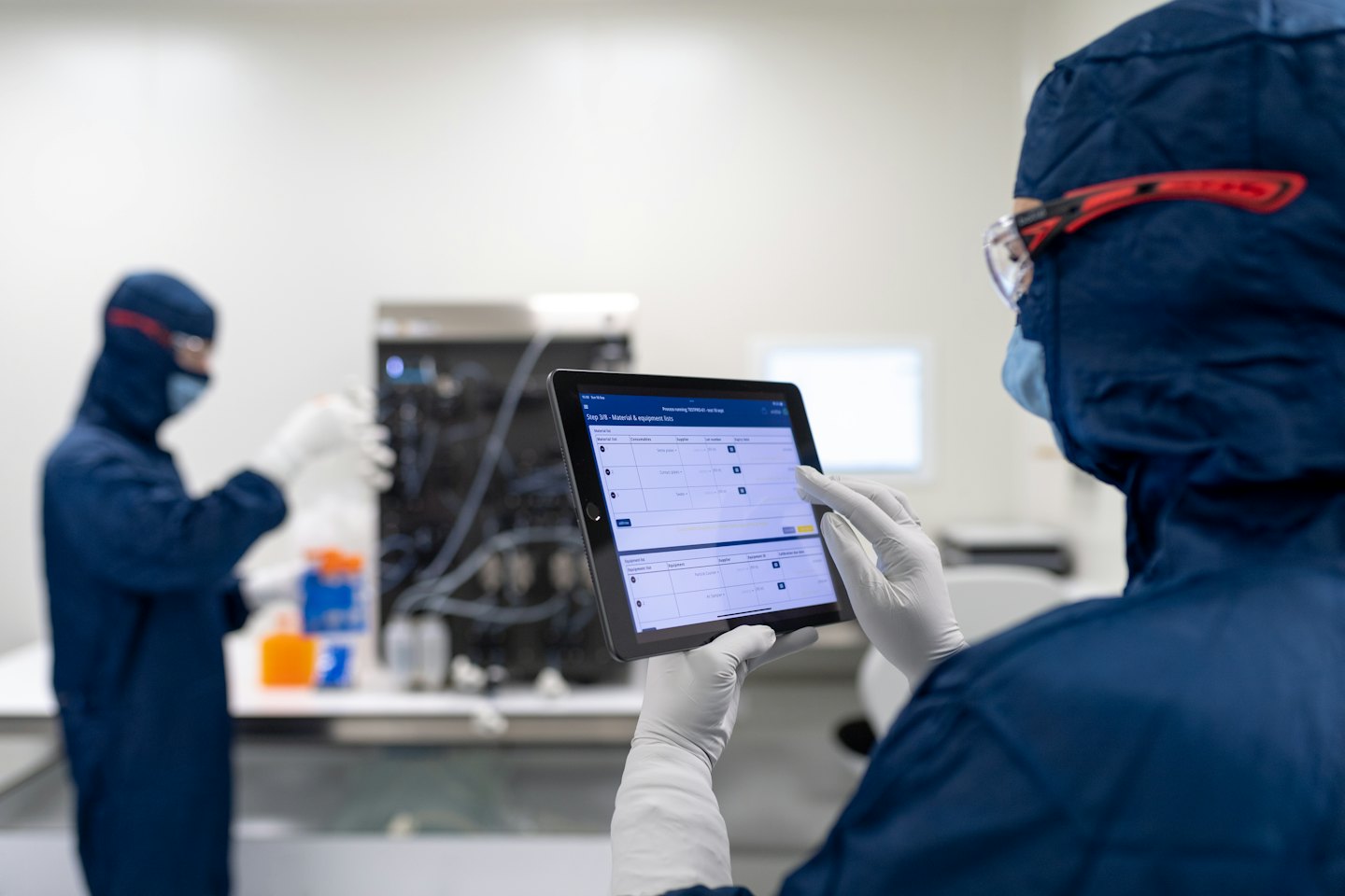 Scienziati in tute da camera bianca esaminano le pianificazioni di elaborazione su un tablet.